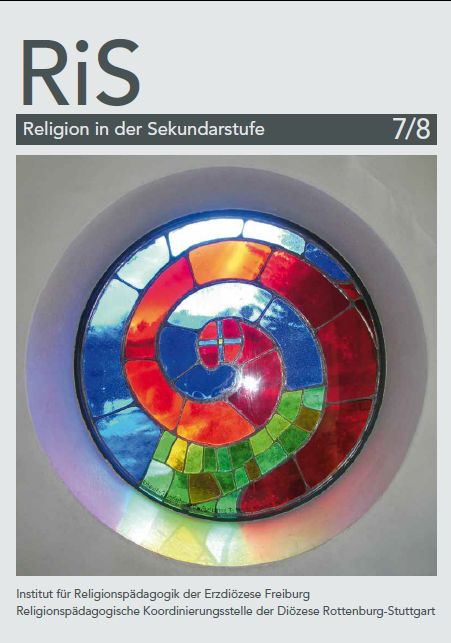 In der Mitte ist ein großes Bild. Auf dem Bild ist ein kleines rundes Fenster zu sehen. Das Fenster besteht aus kleinen bunten Glasteilen. Rote Glasteile laufen spiralförmig in die Mitte des Fensters. Dazwischen sind blaue und grüne Glasteile angeordnet.