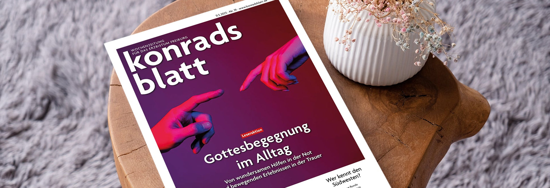 Konradsblatt-Ausgabe mit dem Titelthema „Gottesbegegnung im Alltag“, dekorativ auf einem Holztisch mit Blumenvase präsentiert